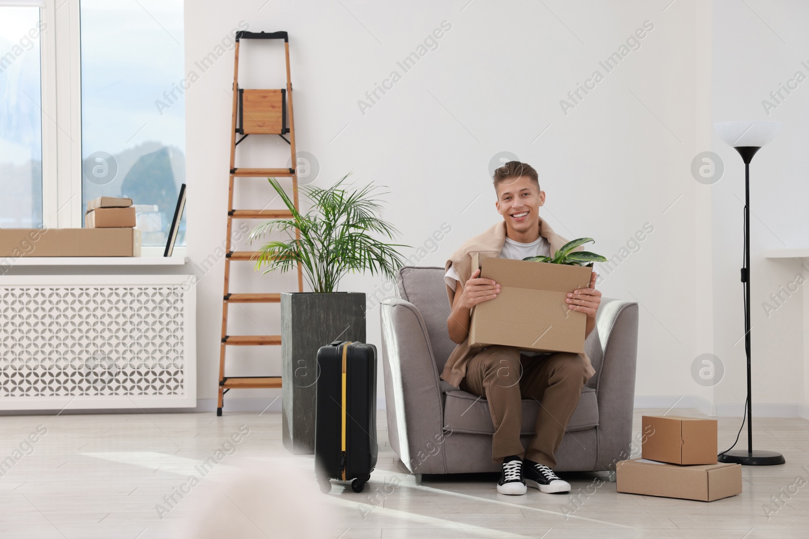 Photo of Happy man with moving boxes and suitcase in new apartment. Housewarming party