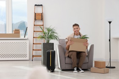 Happy man with moving boxes and suitcase in new apartment. Housewarming party