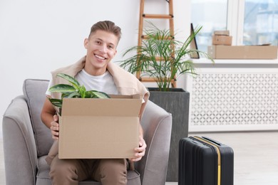 Photo of Happy man holding moving box with houseplant in new apartment. Housewarming party