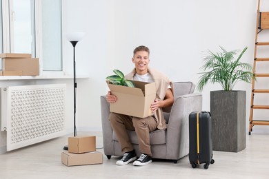 Photo of Happy man with moving boxes and suitcase in new apartment. Housewarming party