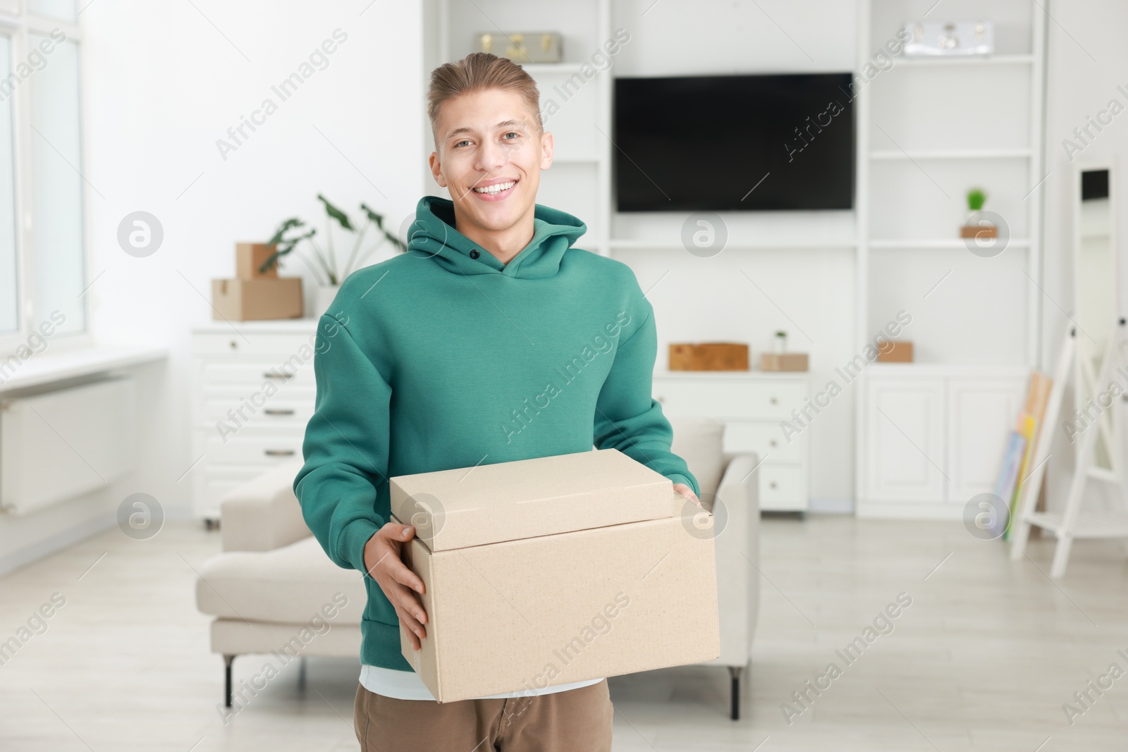 Photo of Happy man with moving boxes in new apartment. Housewarming party