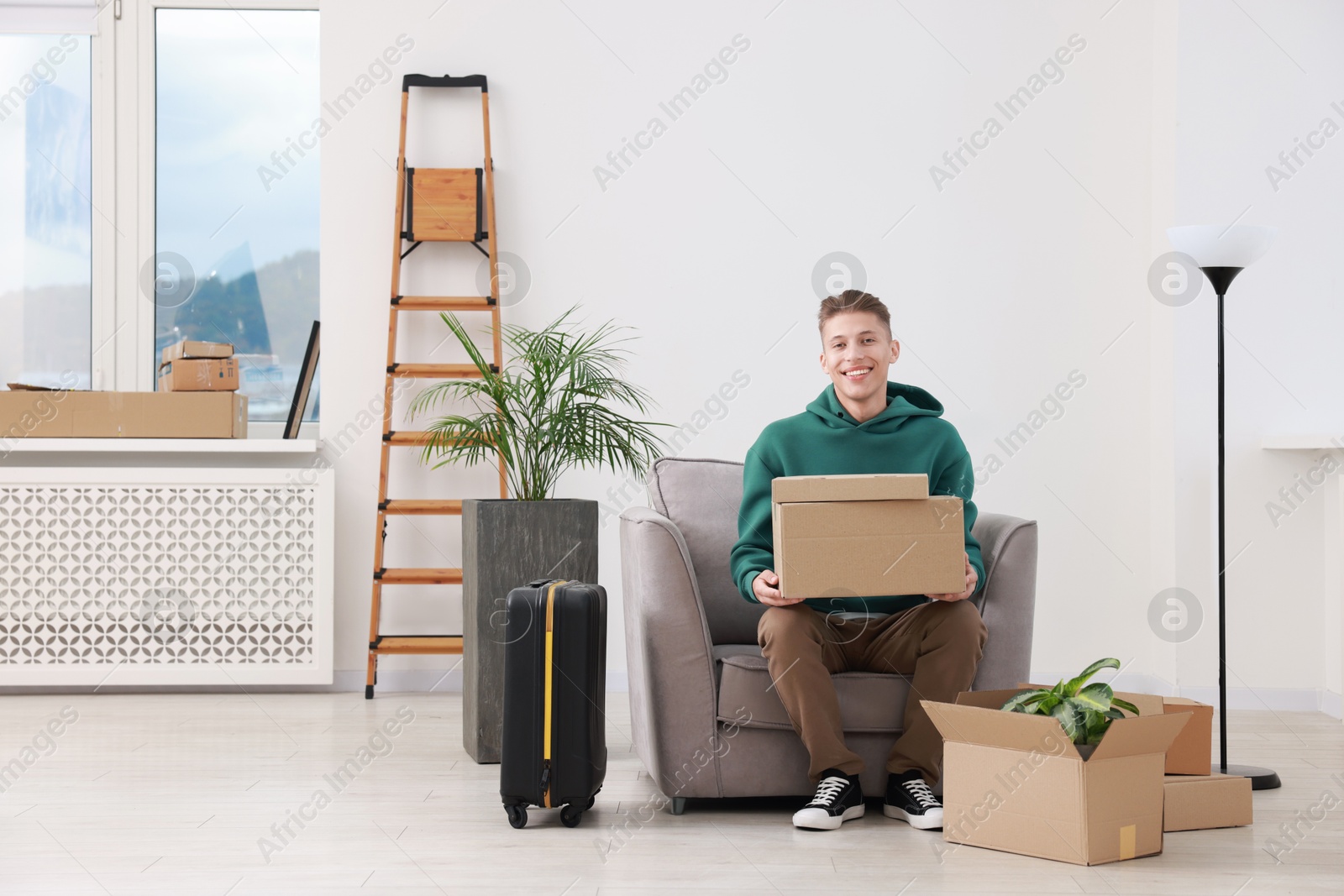 Photo of Happy man with moving boxes and suitcase in new apartment. Housewarming party