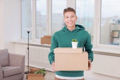 Photo of Happy man with moving boxes and houseplant in new apartment. Housewarming party