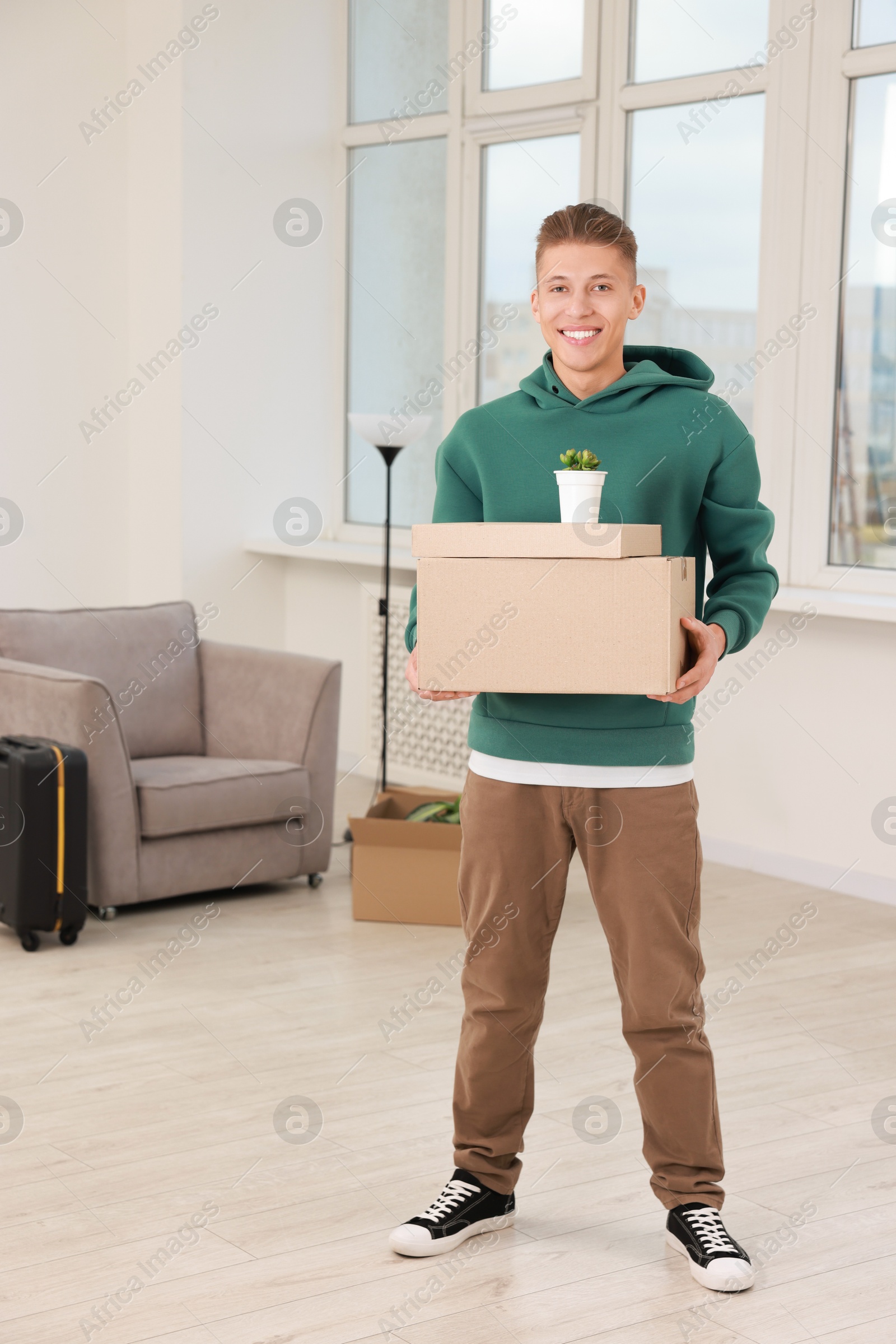 Photo of Happy man with moving boxes and houseplant in new apartment. Housewarming party