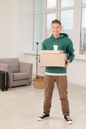 Photo of Happy man with moving boxes and houseplant in new apartment. Housewarming party