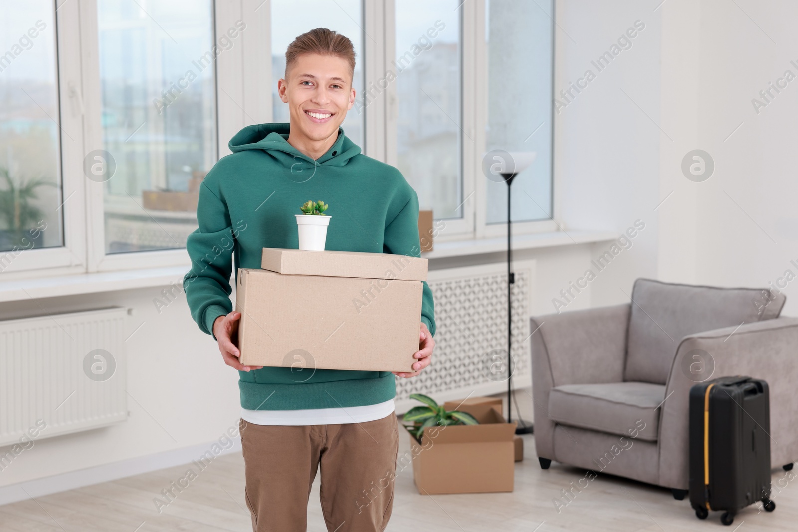 Photo of Happy man with moving boxes and houseplant in new apartment. Housewarming party