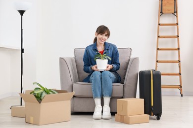 Happy woman with houseplant, moving boxes and suitcase in new apartment. Housewarming party