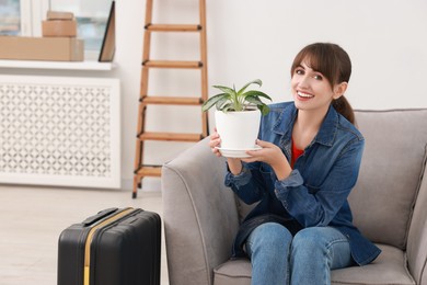 Photo of Happy woman with houseplant and suitcase in new apartment. Housewarming party