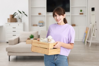 Happy woman holding wooden crate with stuff in new apartment. Housewarming party