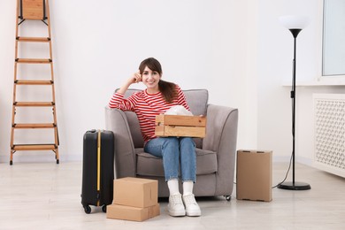 Happy woman with moving boxes and suitcase in new apartment. Housewarming party