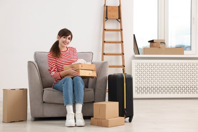 Photo of Happy woman with moving boxes and suitcase in new apartment. Housewarming party