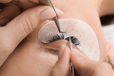 Photo of Woman undergoing lash extensions procedure in beauty salon, closeup