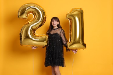 Photo of Coming of age party - 21st birthday. Young woman holding number shaped balloons on yellow background