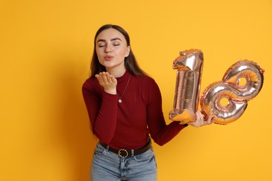 Photo of Coming of age party - 18th birthday. Happy young woman with number shaped balloons blowing kiss on yellow background