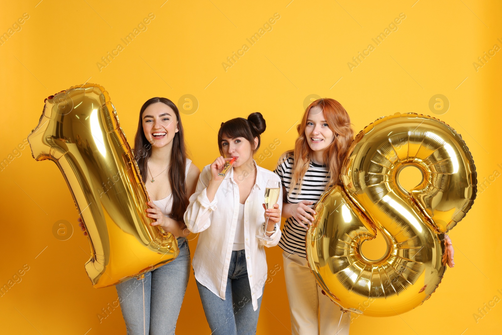 Photo of Coming of age party - 18th birthday. Group of young women celebrating with number shaped balloons on yellow background