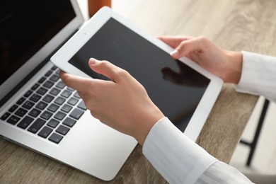 Photo of Businesswoman using tablet at wooden table indoors, closeup. Modern technology