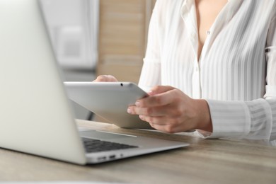 Photo of Businesswoman using tablet at wooden table indoors, closeup. Modern technology