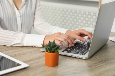 Photo of Businesswoman using laptop at wooden table indoors, closeup. Modern technology