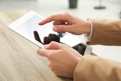 Photo of Businesswoman using tablet at wooden table indoors, closeup. Modern technology