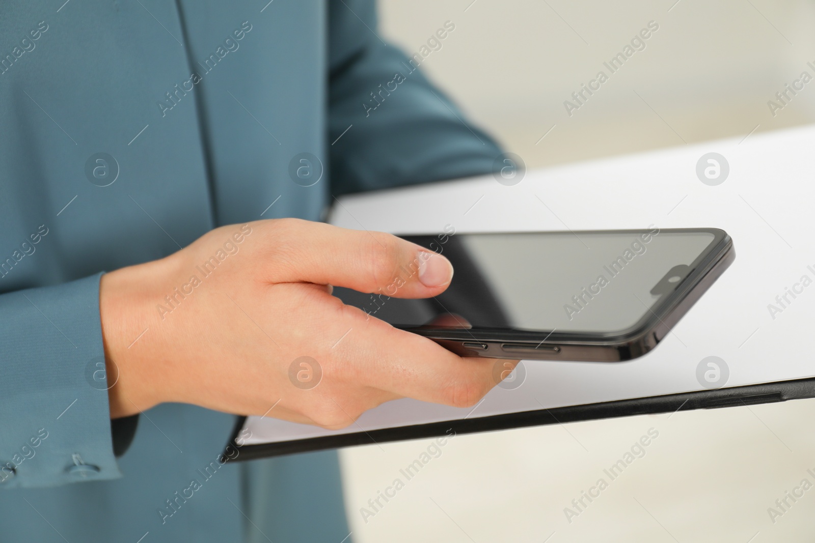 Photo of Businesswoman with clipboard using smartphone indoors, closeup. Modern technology