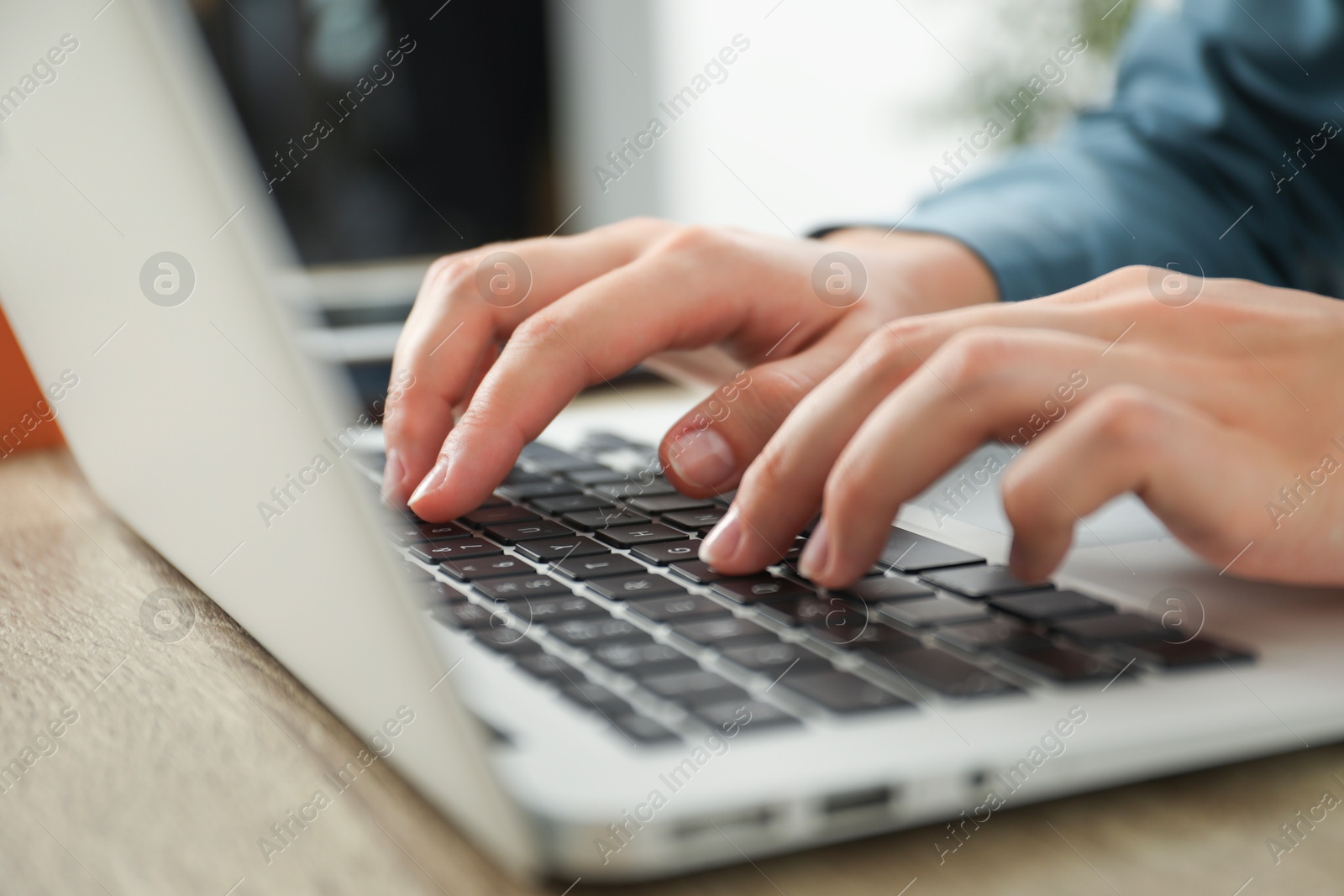 Photo of Businesswoman using laptop at wooden table indoors, closeup. Modern technology