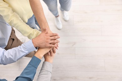 Photo of Teamwork. Group of employees joining hands in office, top view. Space for text