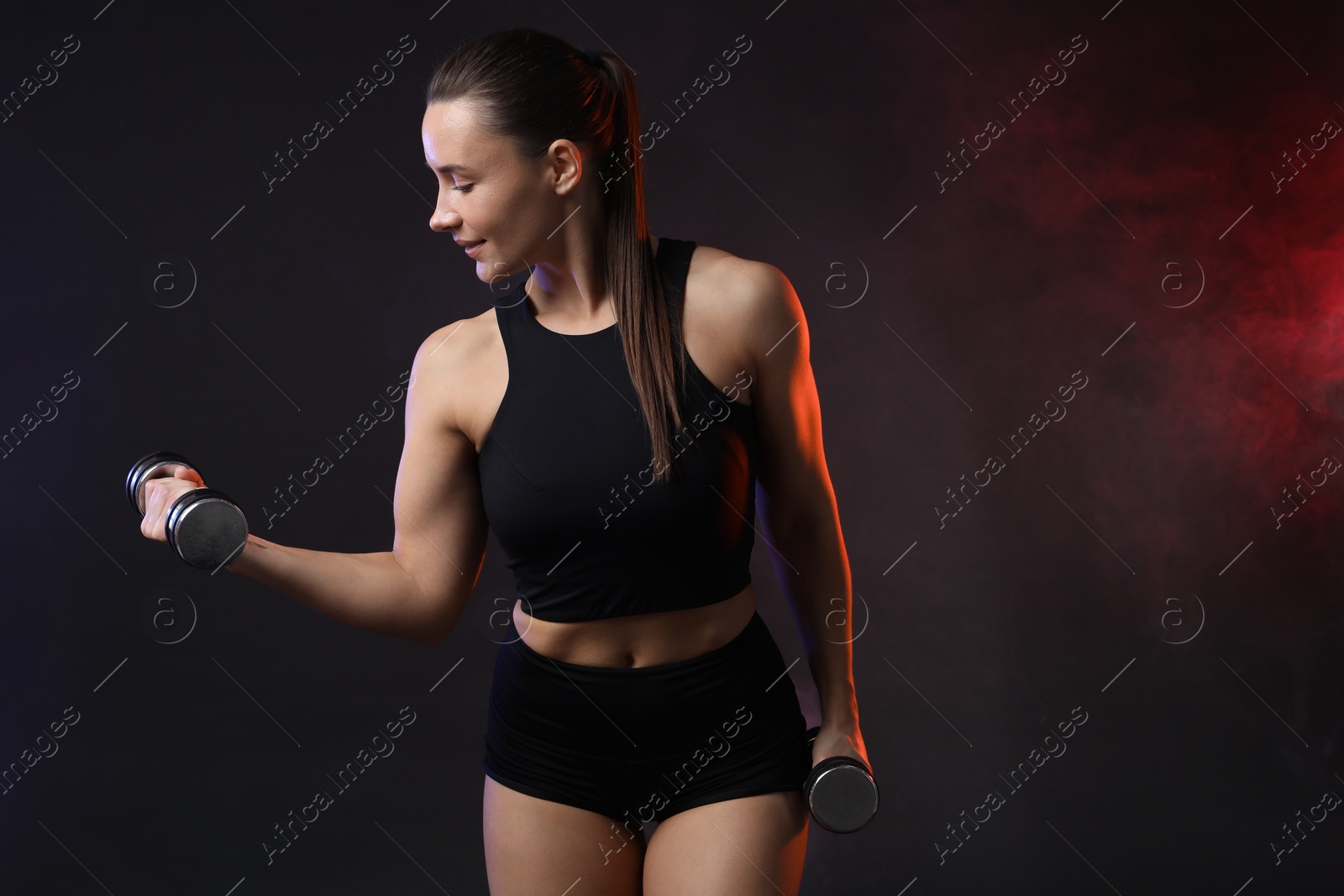 Photo of Woman exercising with dumbbells in smoke on dark background