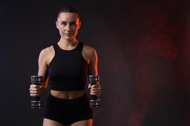 Photo of Woman exercising with dumbbells in smoke on dark background, space for text