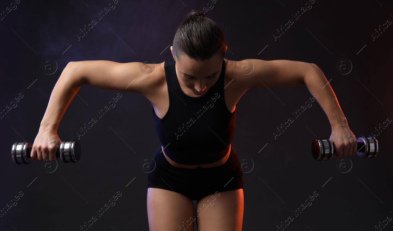 Photo of Woman exercising with dumbbells in smoke on dark background