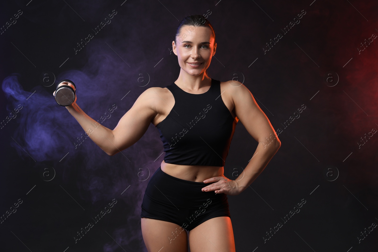 Photo of Woman exercising with dumbbell in smoke on dark background