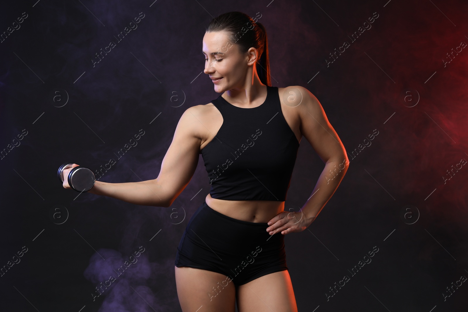 Photo of Woman exercising with dumbbell in smoke on dark background