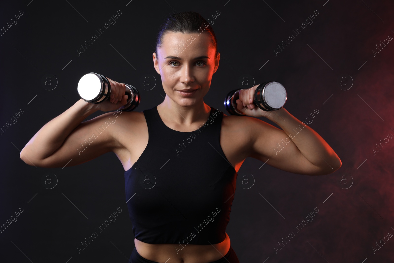 Photo of Woman exercising with dumbbells in smoke on dark background