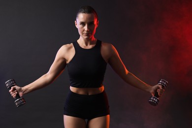 Woman exercising with dumbbells in smoke on dark background