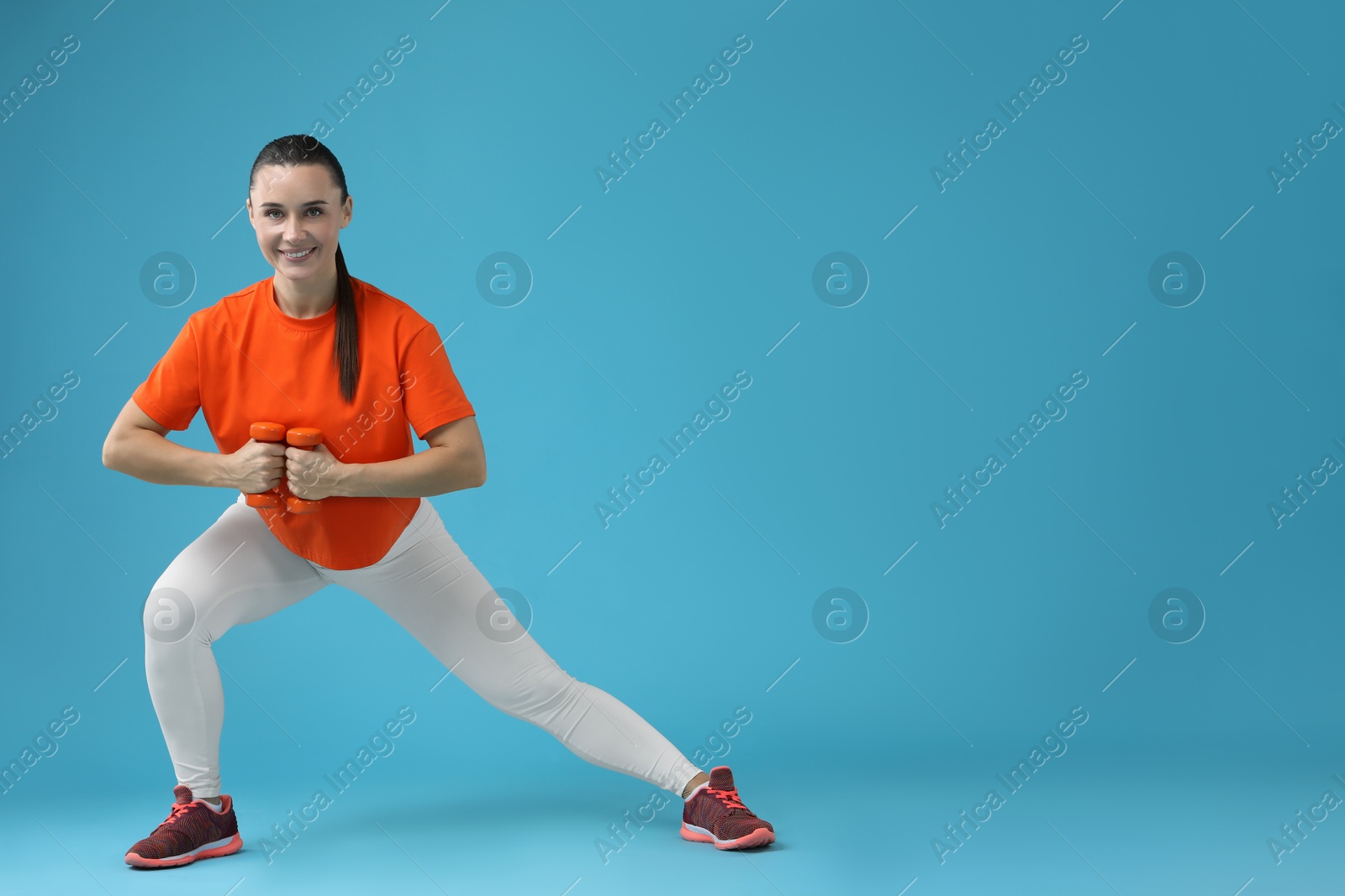 Photo of Woman exercising with dumbbells on light blue background, space for text