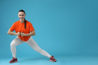 Woman exercising with dumbbells on light blue background, space for text