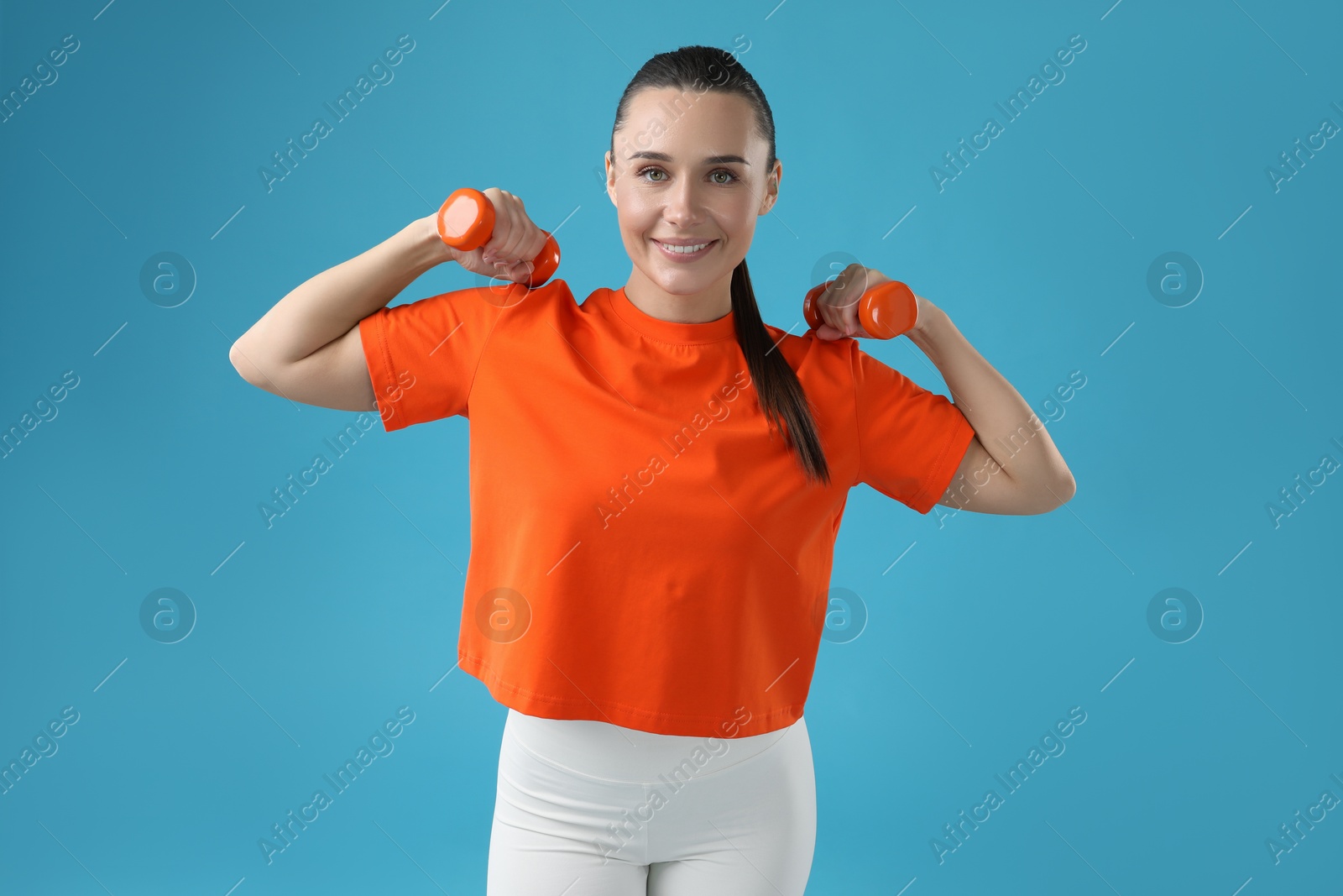 Photo of Woman exercising with dumbbells on light blue background