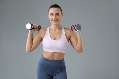 Woman exercising with dumbbells on light grey background