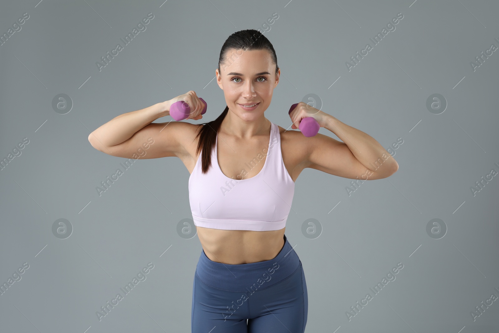 Photo of Woman exercising with dumbbells on light grey background