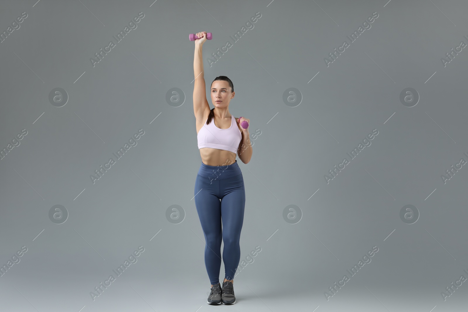 Photo of Woman exercising with dumbbells on light grey background