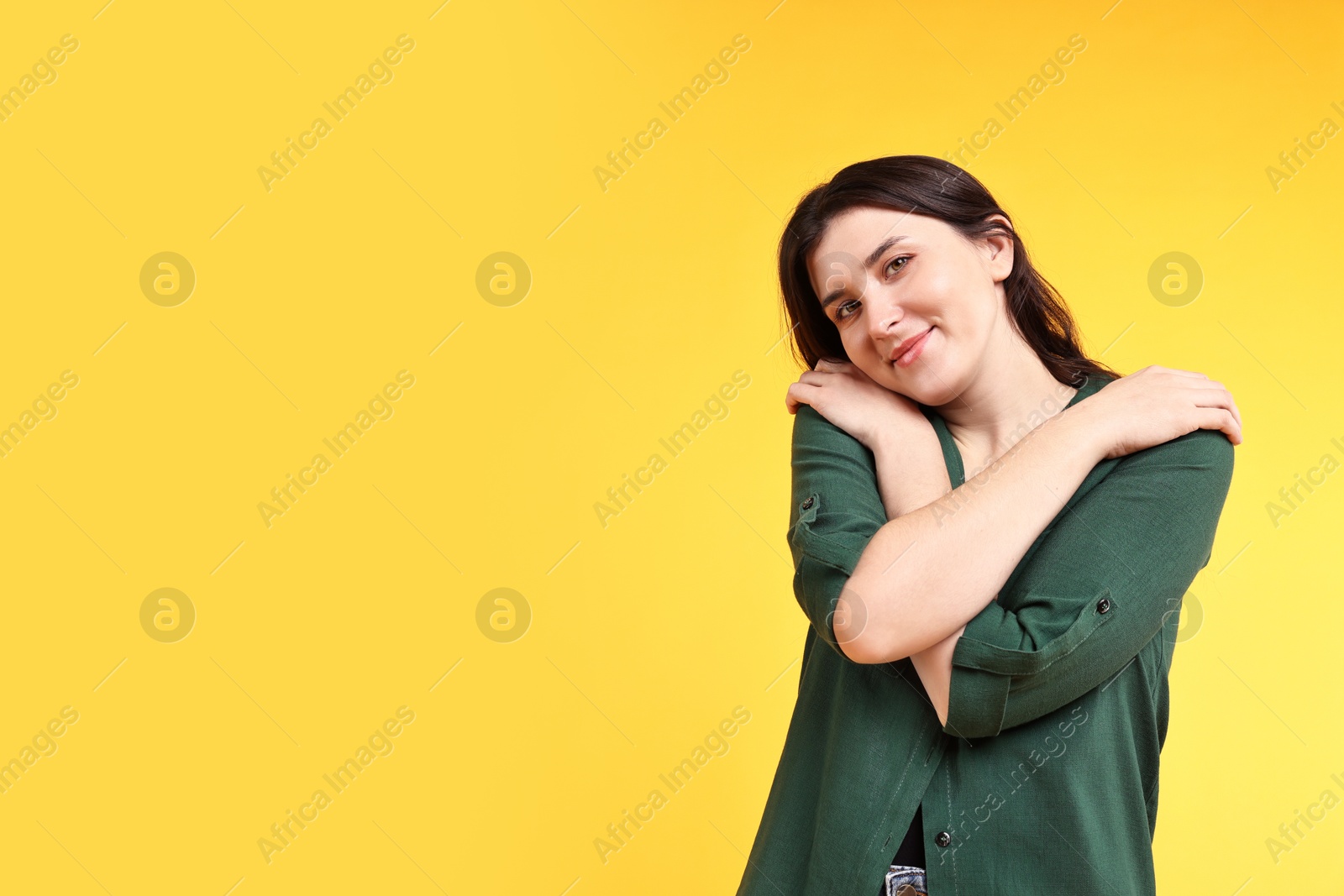 Photo of Beautiful young woman hugging herself on yellow background, space for text