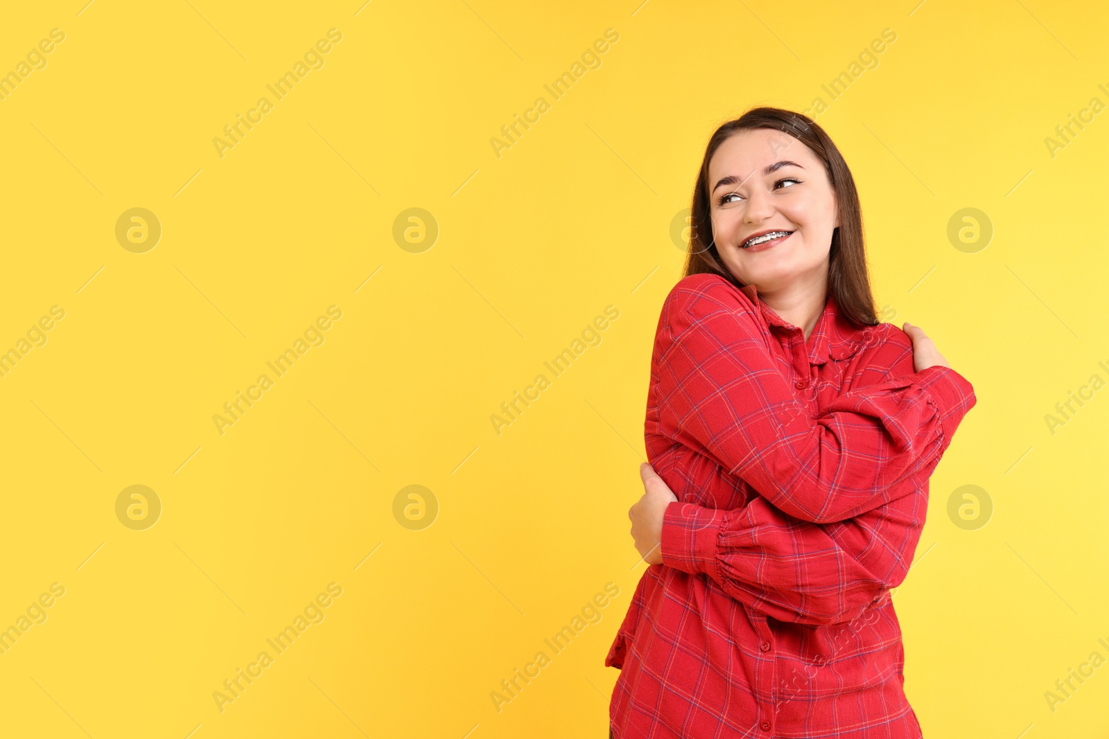 Photo of Beautiful young woman hugging herself on yellow background, space for text