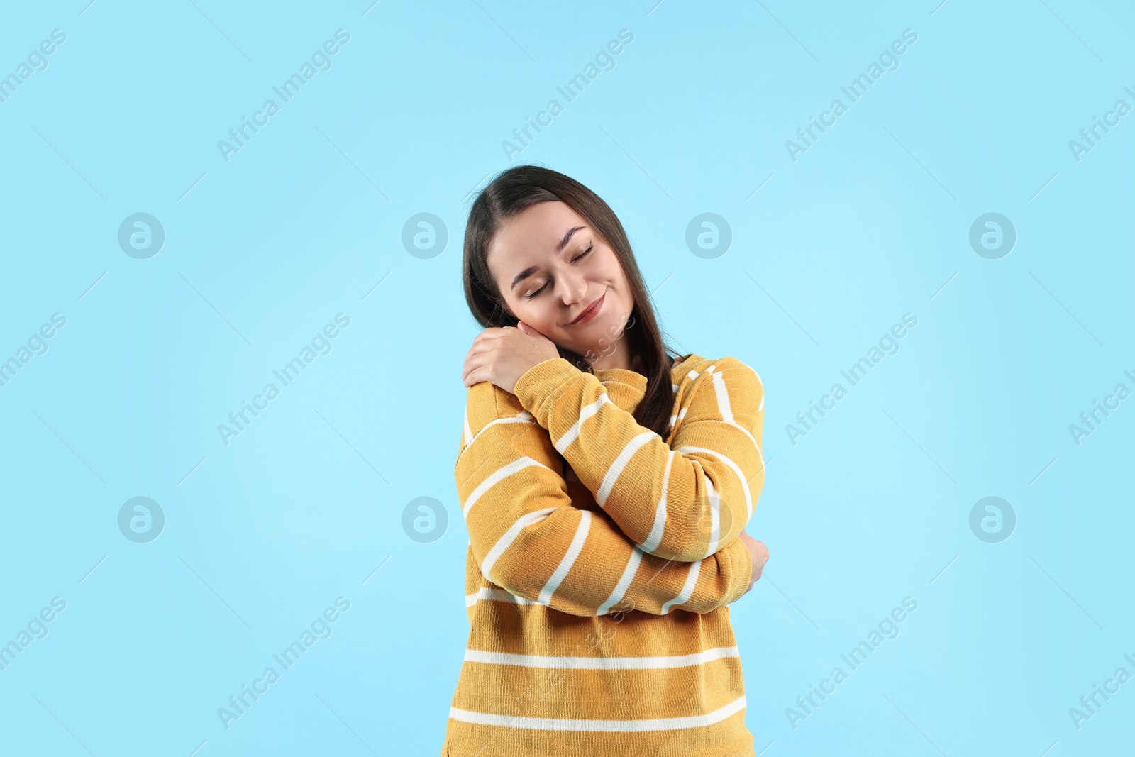 Photo of Beautiful young woman hugging herself on light blue background