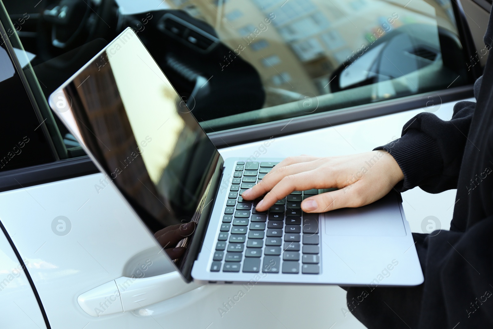 Photo of Thief hacking car system with laptop near vehicle, closeup