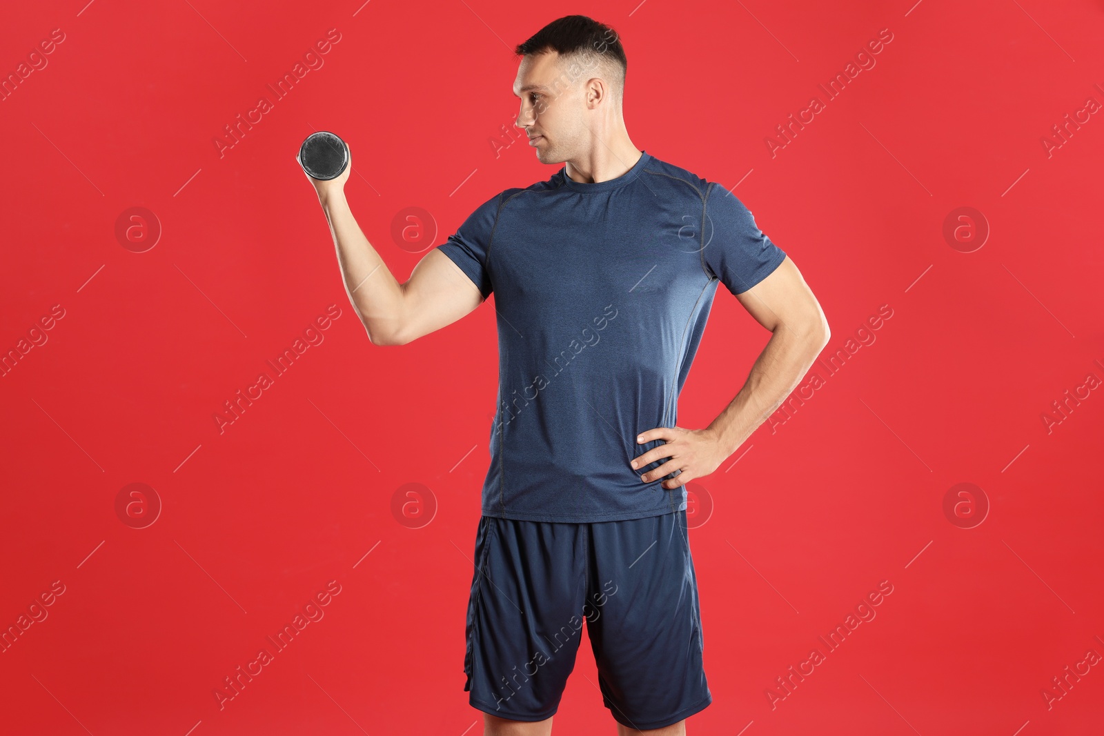 Photo of Man exercising with dumbbell on red background