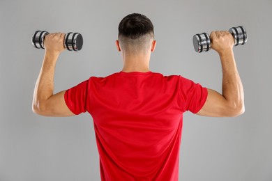 Photo of Man exercising with dumbbells on grey background, back view