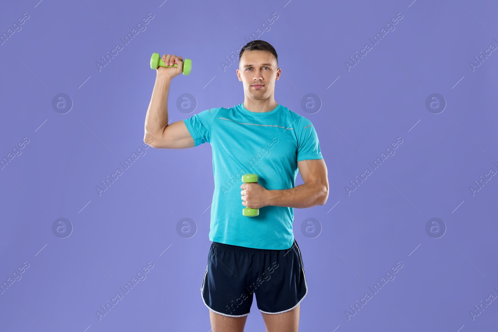 Photo of Man exercising with dumbbells on violet background