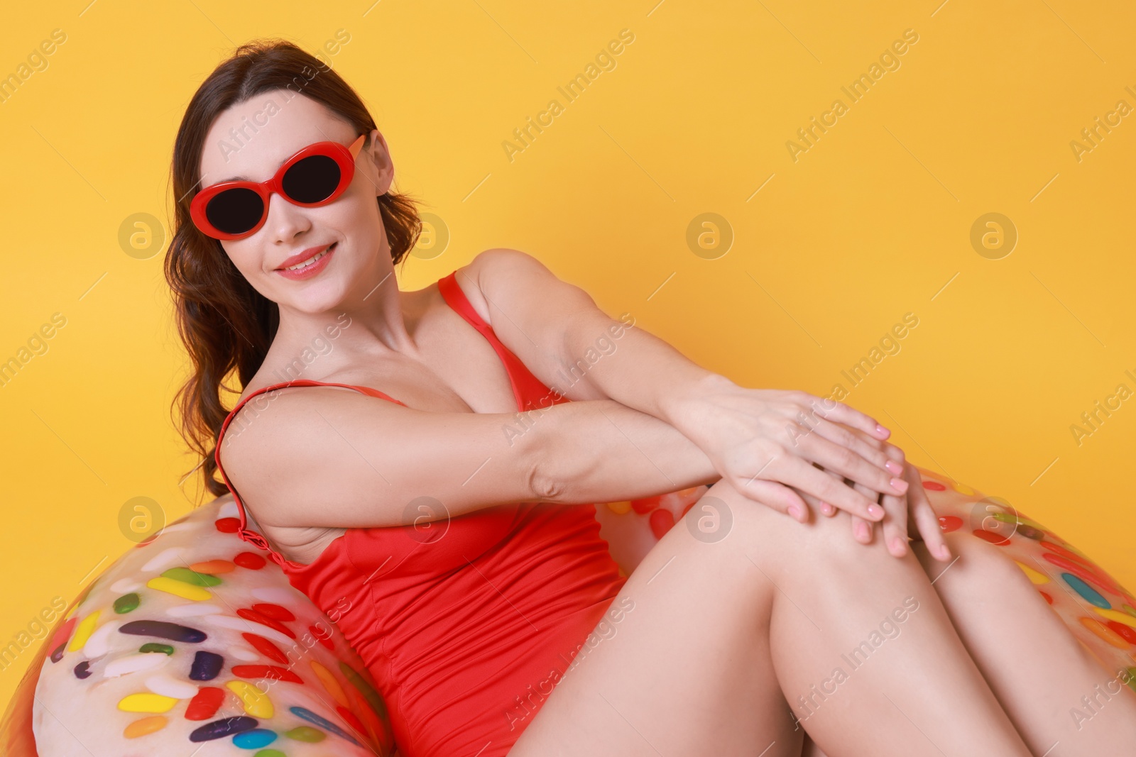 Photo of Beautiful woman in swimsuit with inflatable ring on yellow background