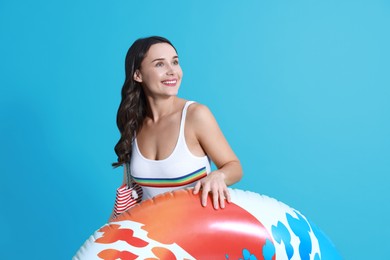 Beautiful woman in swimsuit with inflatable ring on light blue background