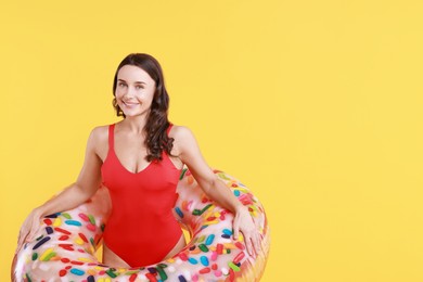 Photo of Beautiful woman in swimsuit with inflatable ring on yellow background. Space for text