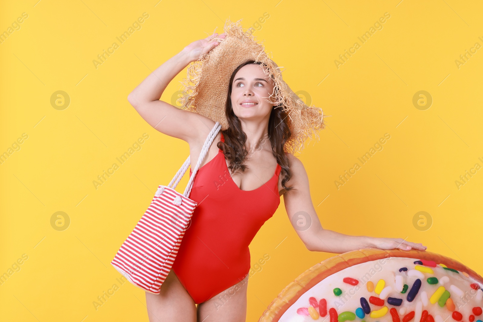 Photo of Beautiful woman wearing swimsuit and straw hat with inflatable ring on yellow background